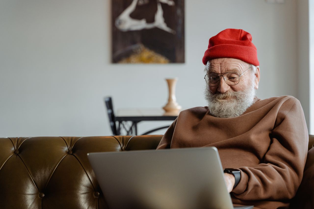 Um senhor sorrindo enquanto usa um notebook na sala de casa